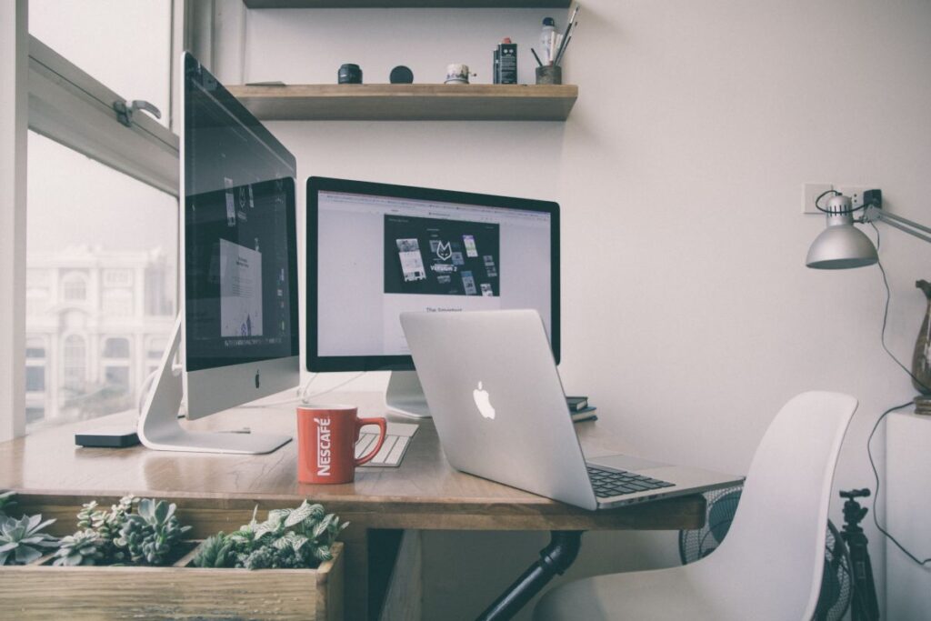 A wide horizontal featured layout showing a compact dual monitor desk setup for high income remote software engineers in a small apartment.